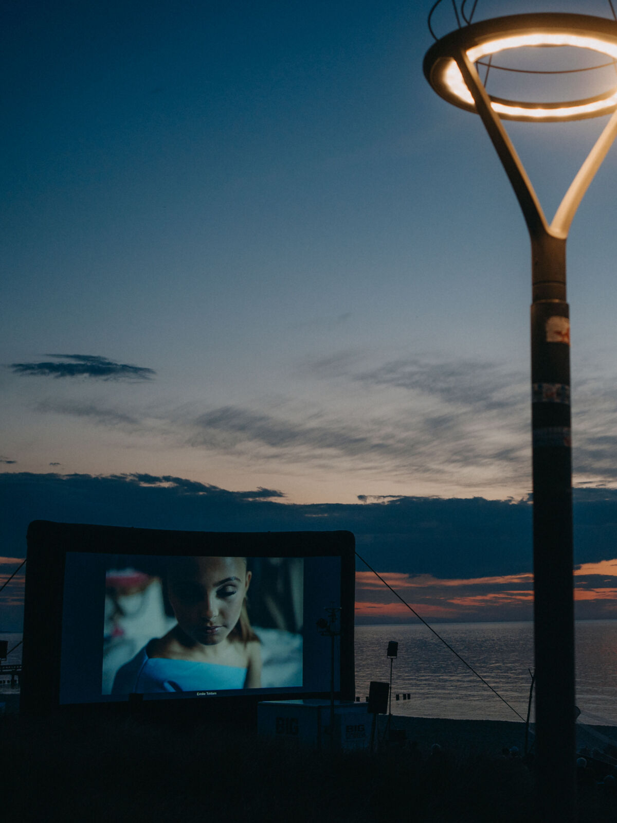 Am Strand steht eine große Leinwand mit Aufschrift "Umweltfotofestival Zingst". Davor sitzen Menschen in Grüppchen zusammen.