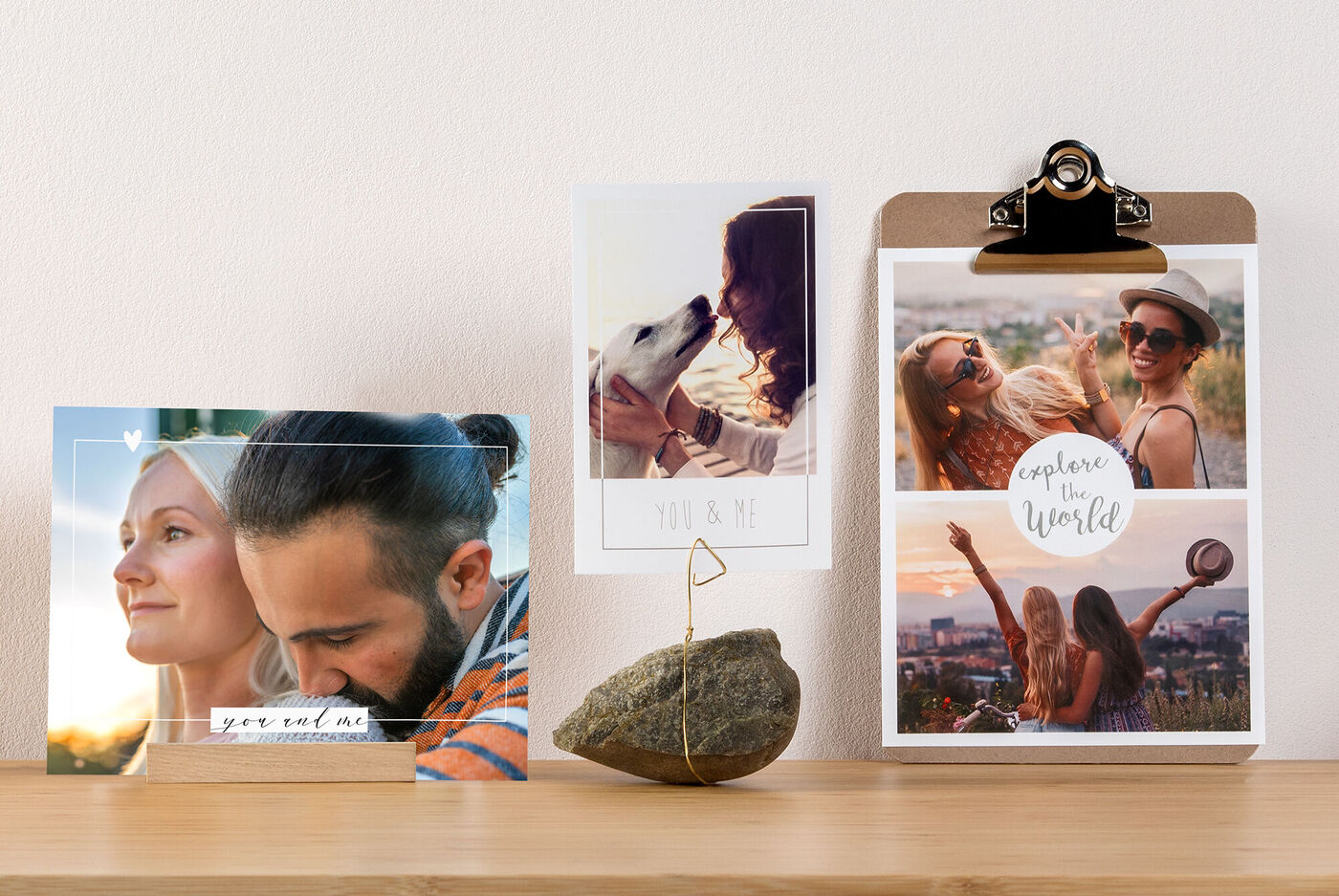 Drei schöne Fotos auf einer Holzoberfläche. Links ein Bild von einer Person und einer Landschaft, in der Mitte ein Bild mit einer Person und einem Hund, rechts zwei Frauen, die zusammen lachen. Über dem rechten Bild steht 'explore your world'